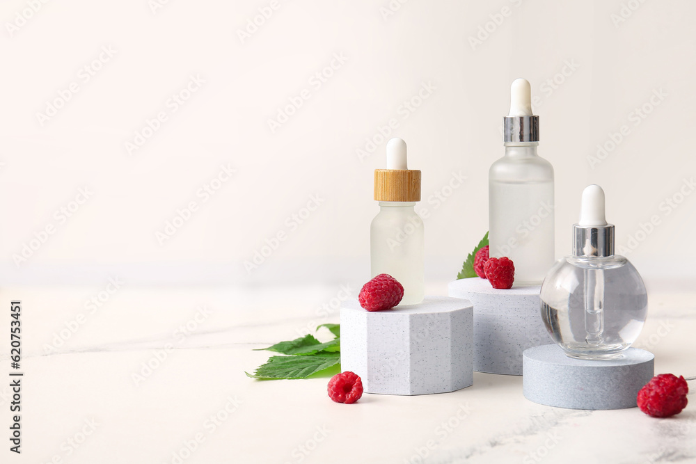 Decorative podiums with bottles of cosmetic raspberry oil on white background