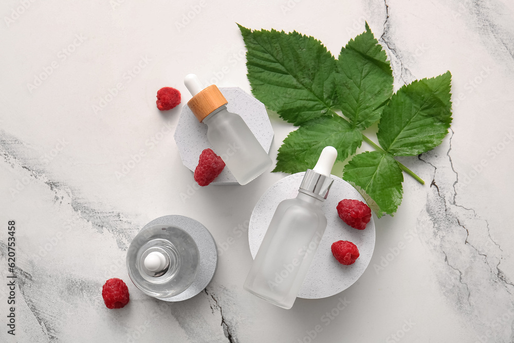 Decorative podiums with bottles of cosmetic raspberry oil on white background