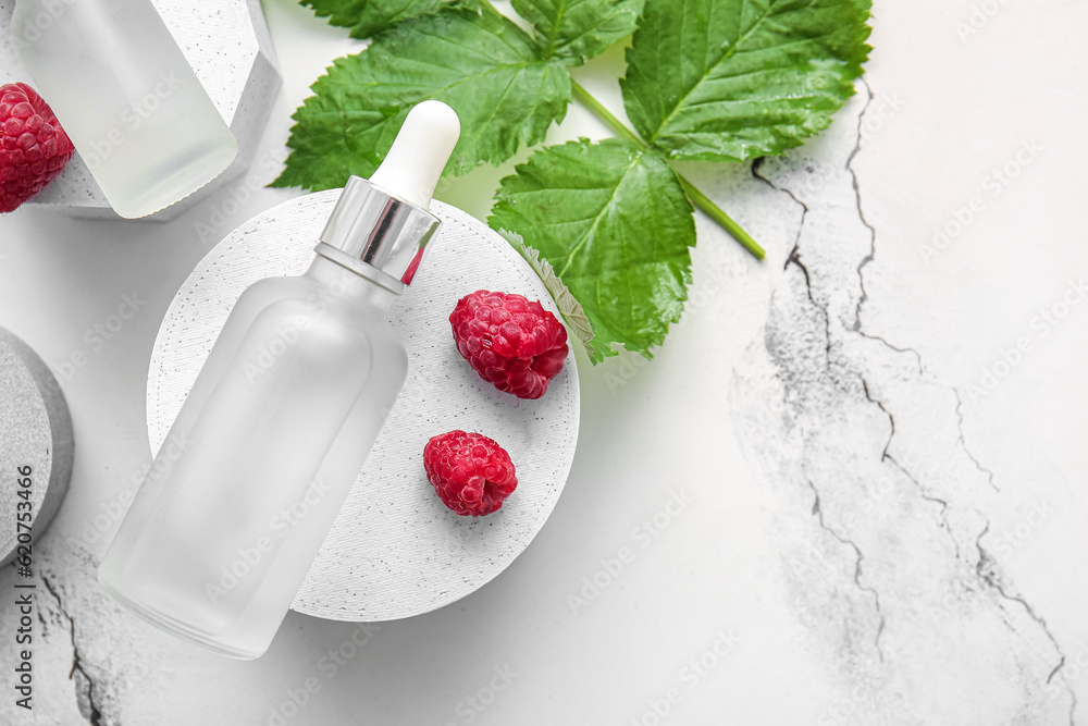 Decorative podium with bottle of cosmetic raspberry oil on white background