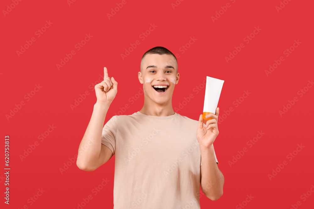 Happy young man with bottle of sunscreen cream on red background