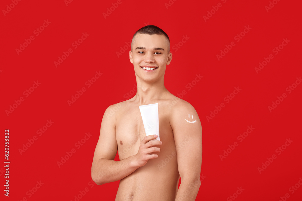 Happy young man with bottle of sunscreen cream on red background