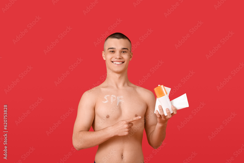 Happy young man pointing at bottles of sunscreen cream on red background