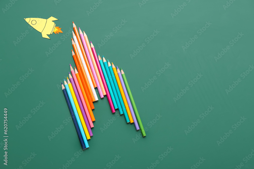 Pencils with paper rocket on green background