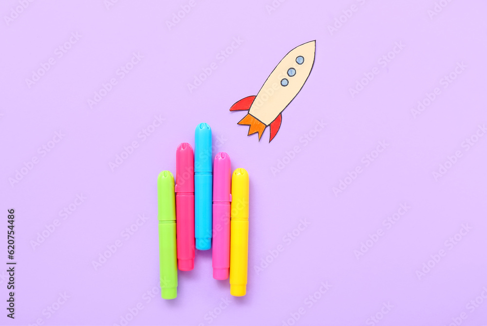 Markers with paper rocket on purple background