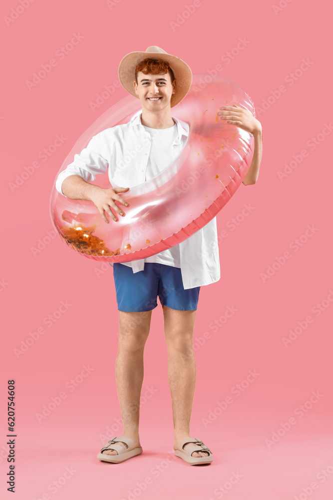 Young man with swim ring on pink background