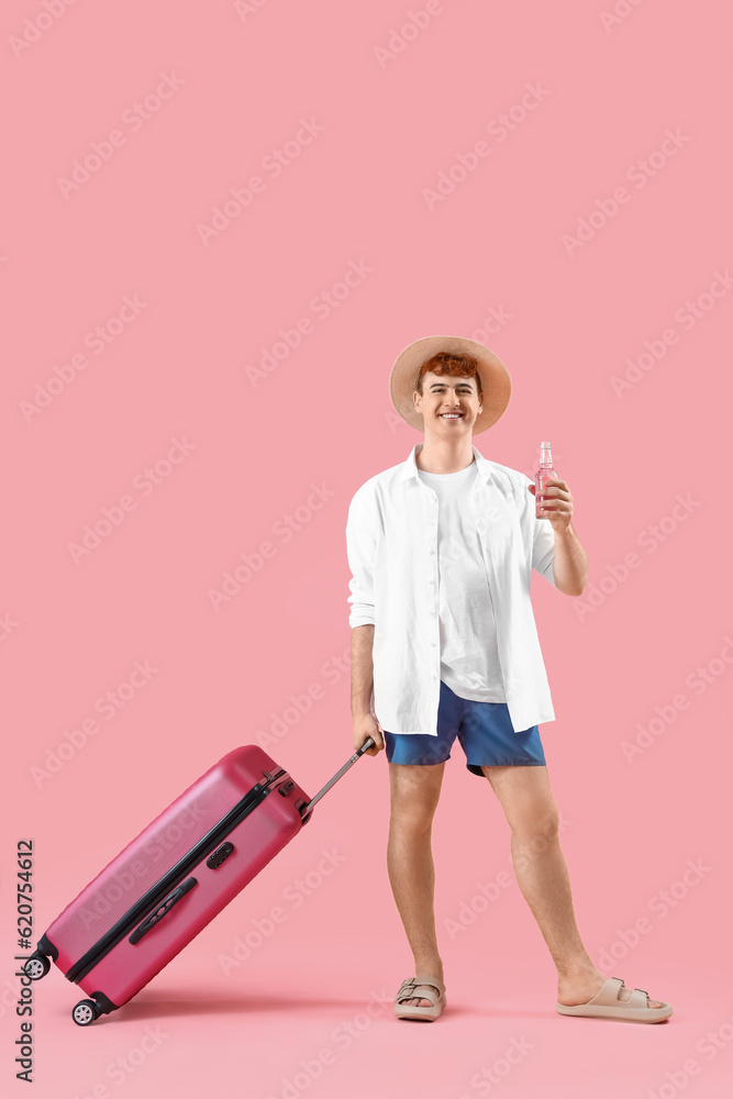 Young man with suitcase on pink background