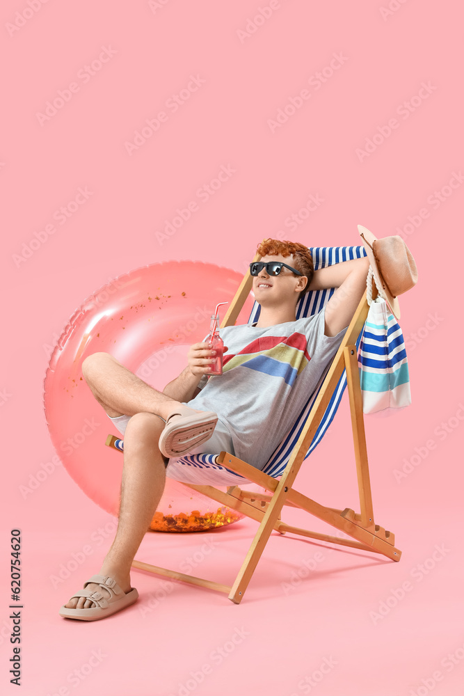 Young man with soda in deck chair on pink background