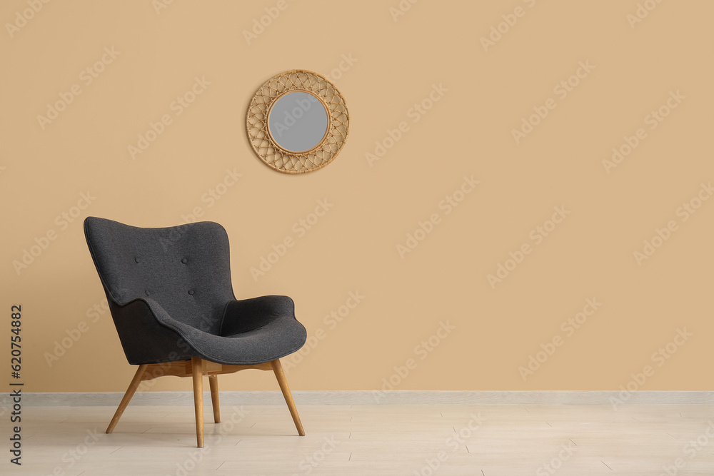 Stylish black armchair and mirror near beige wall