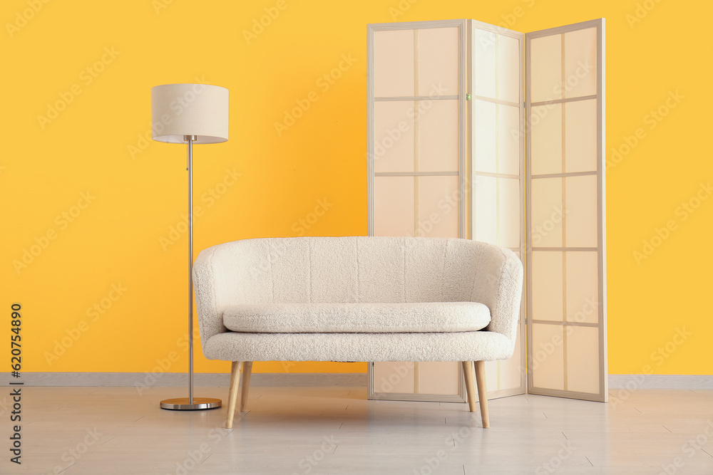 Cozy white sofa with folding screen and lamp near yellow wall