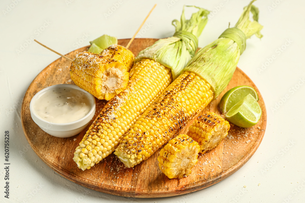 Wooden board with tasty grilled corn cobs and sauce on white background