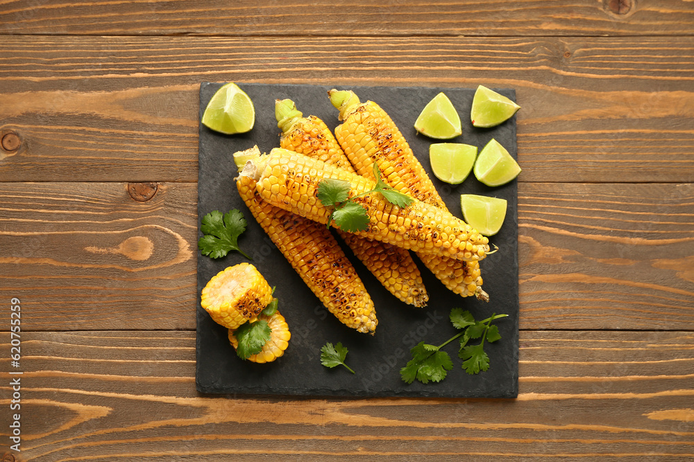 Board with tasty grilled corn cobs and lime on wooden background