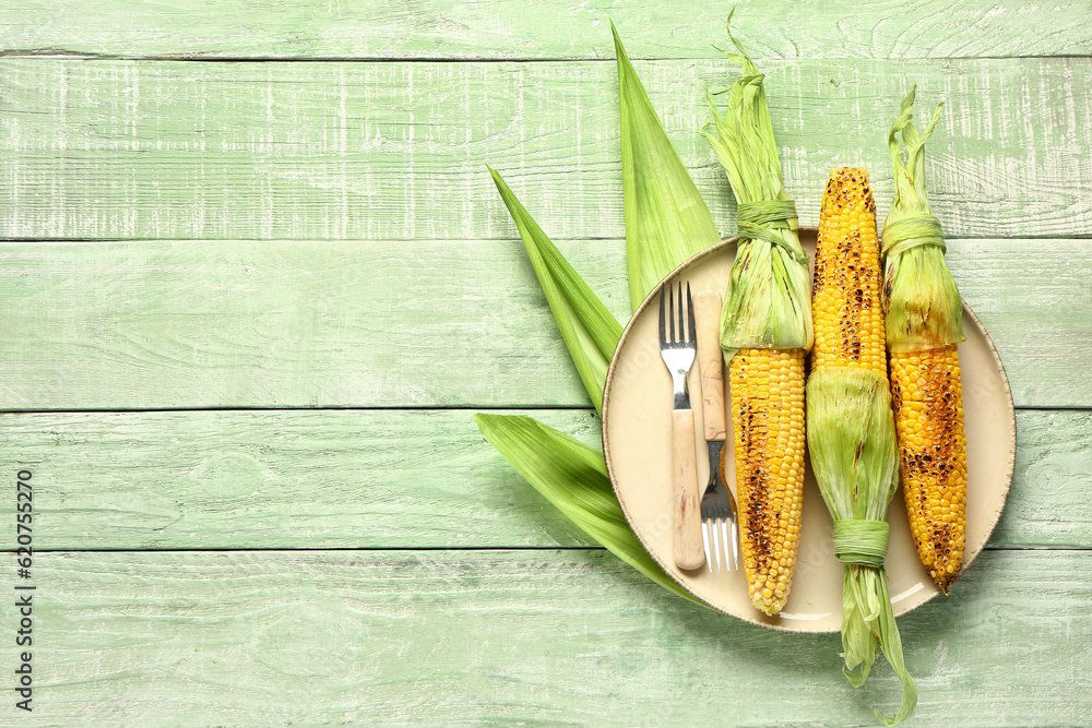 Plate with tasty grilled corn cobs on green wooden background