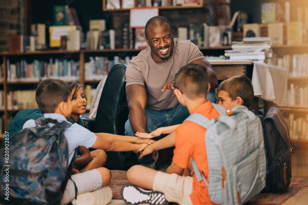 Male school teacher huddling with his students in a library