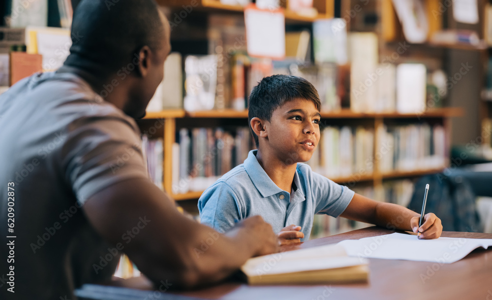 Young school boy having a lesson with his teacher in a library