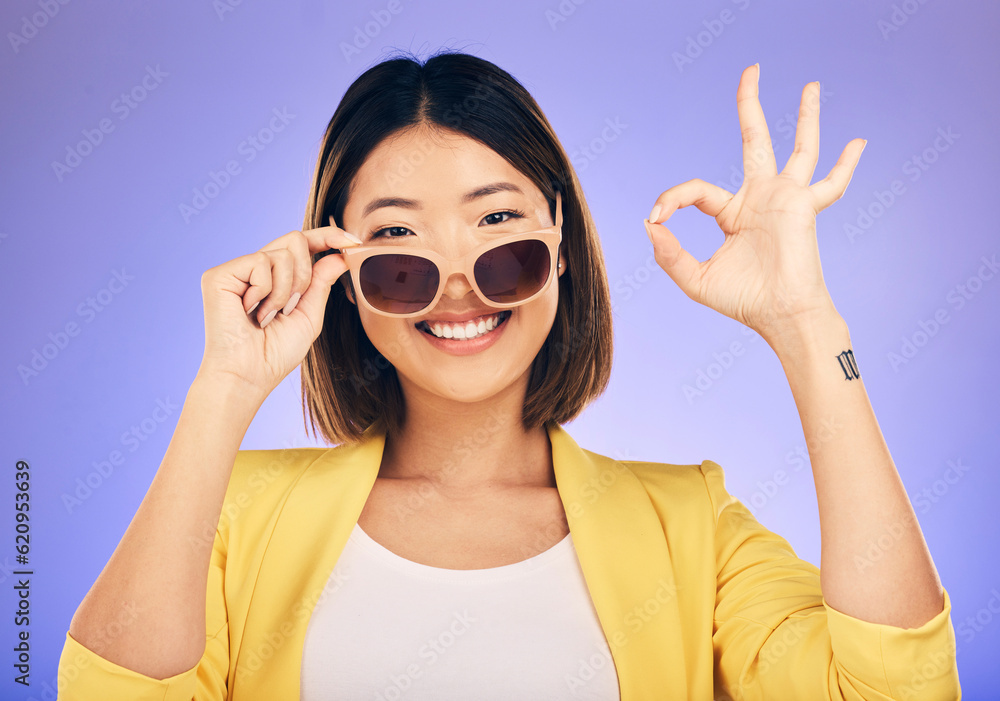 Happy asian woman, portrait and sunglasses, OK sign or fashion accessory against a purple studio bac