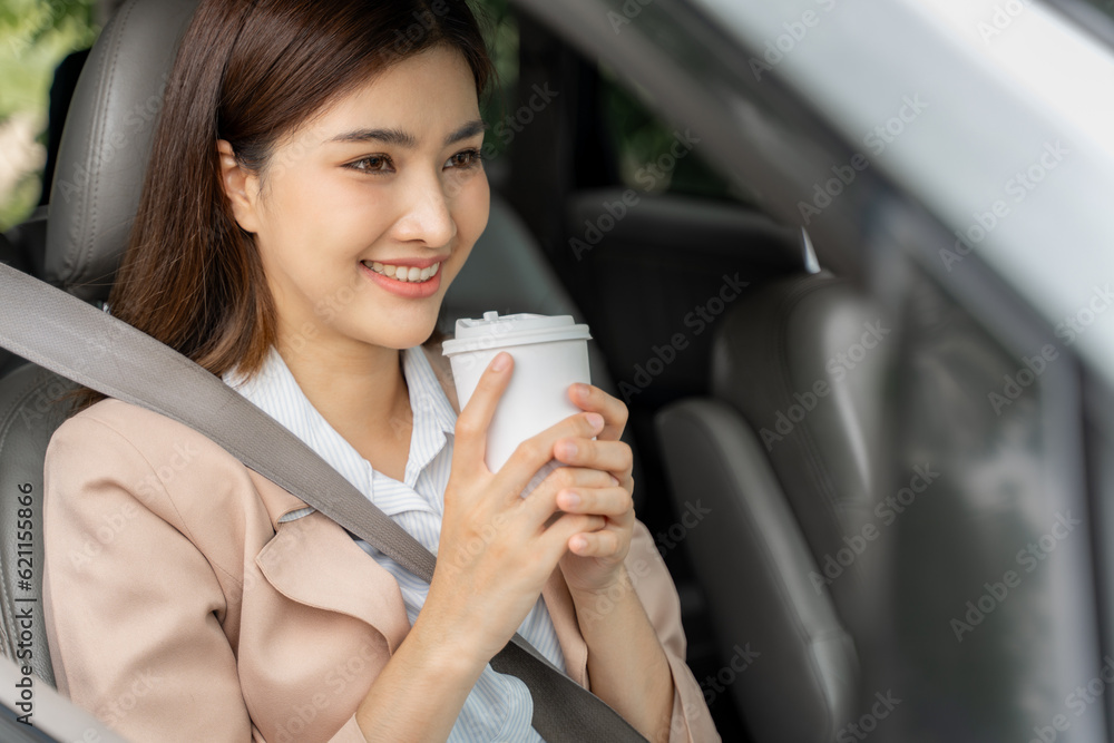 Happy smiling successful young working woman holding take away cup of coffee while sitting in her ca