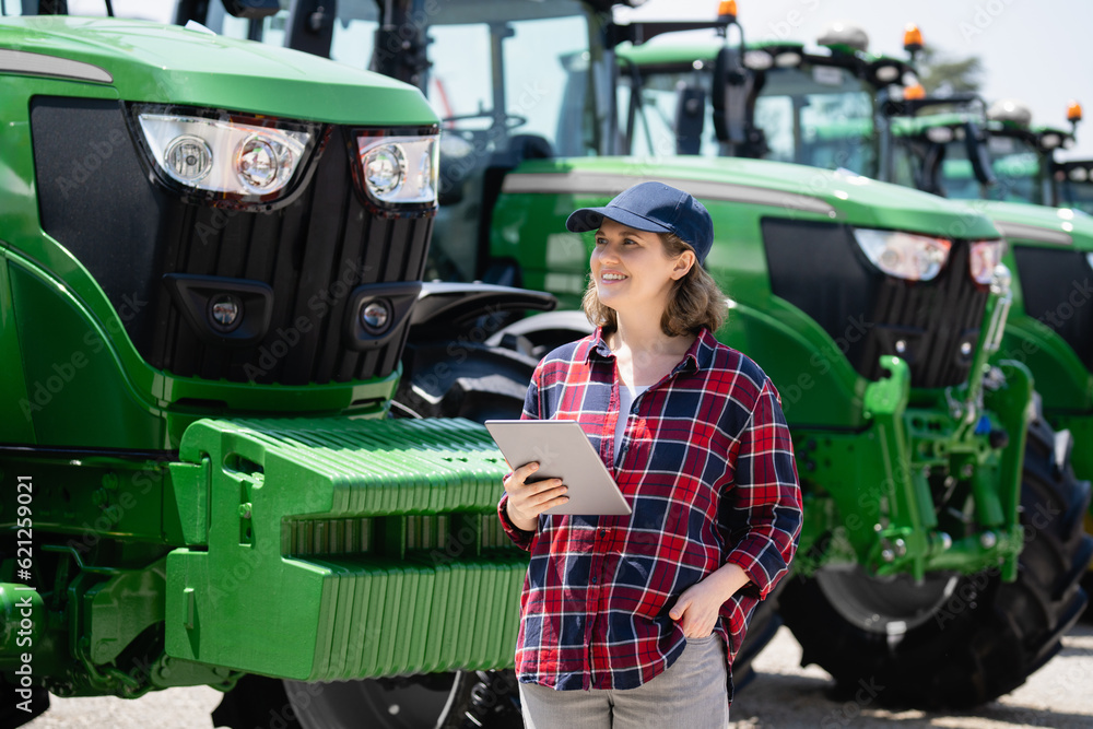 Woman farmer with a digital tablet on the background of an agricultural tractor.s