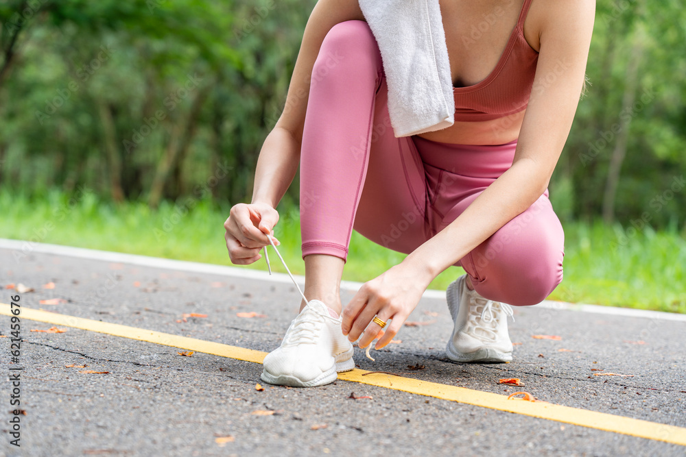 Young attractive Asian woman tying her shoelace before her morning exercise run at running track of 