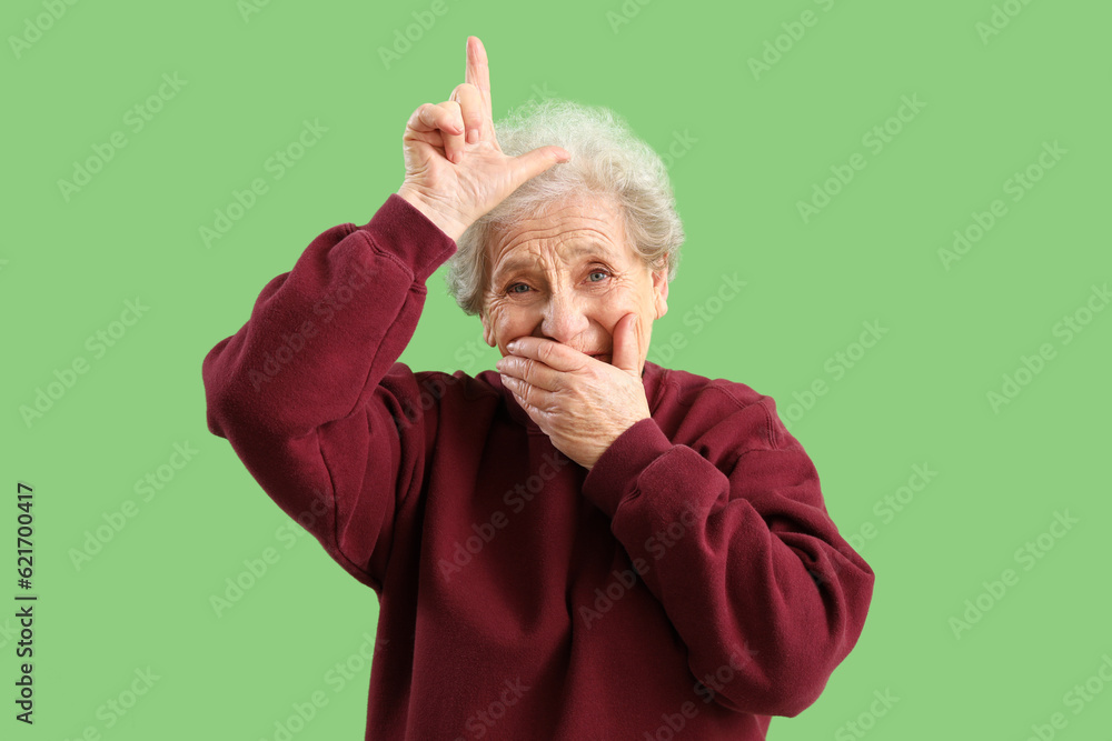 Senior woman showing loser gesture on green background