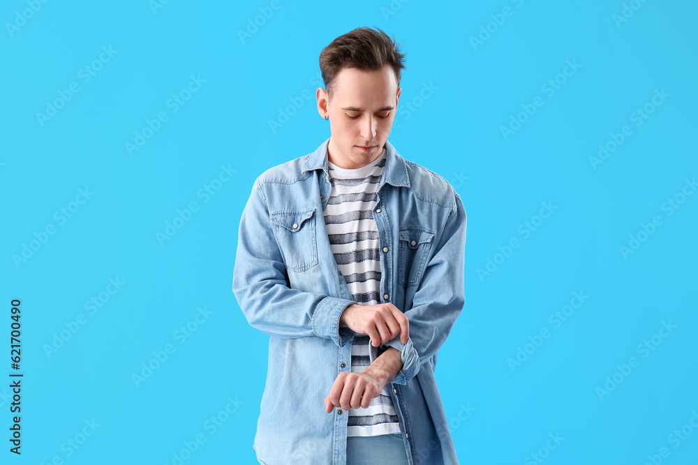 Young man rolling up his sleeve on light blue background