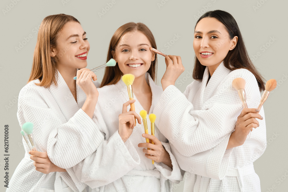 Young women with makeup brushes on grey background