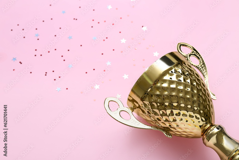 Gold cup with stars on pink background, closeup