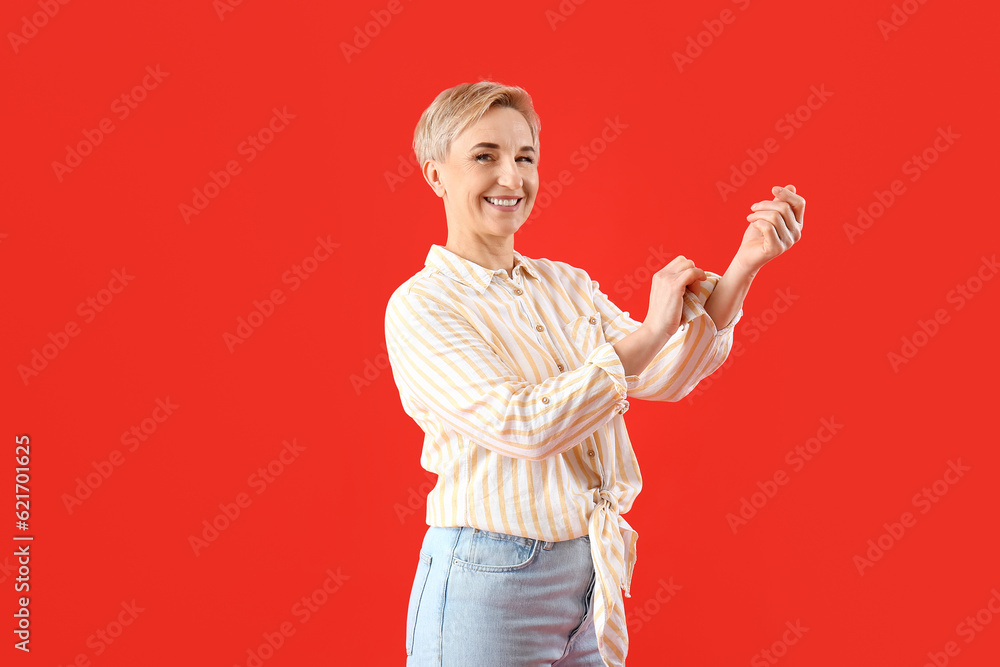 Mature woman rolling up her sleeve on red background