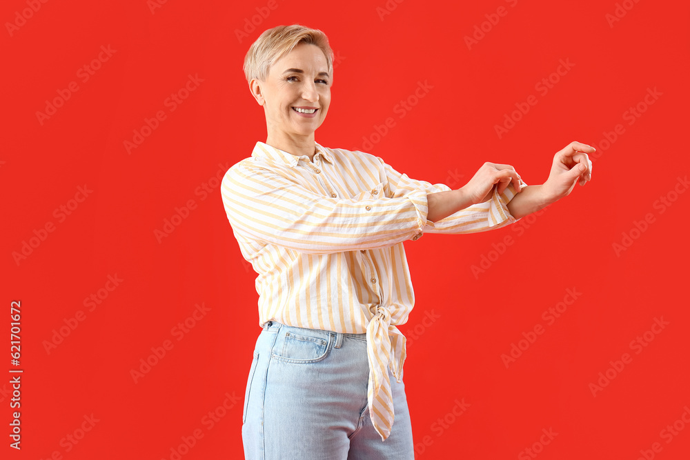 Mature woman rolling up her sleeve on red background