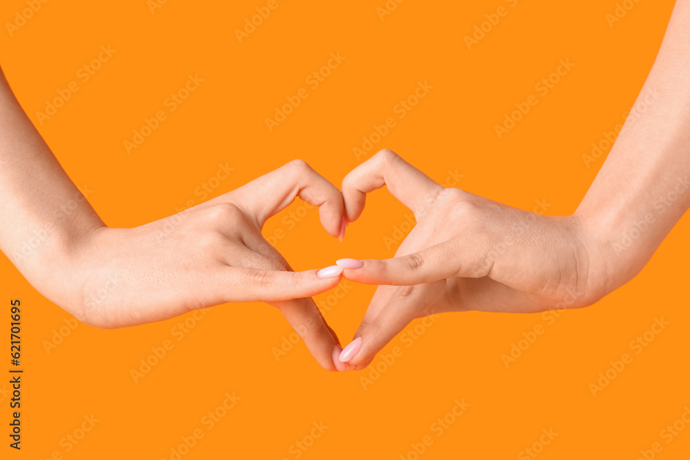 Woman making heart with her hands on orange background