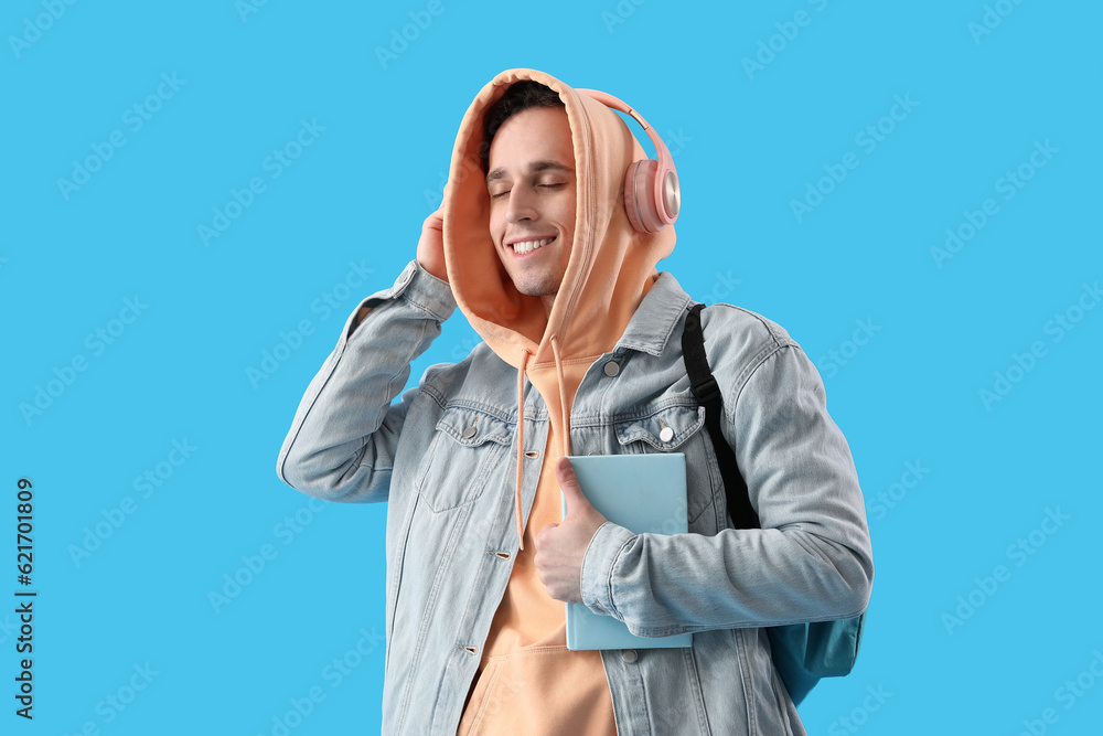 Male student with book listening to music on blue background