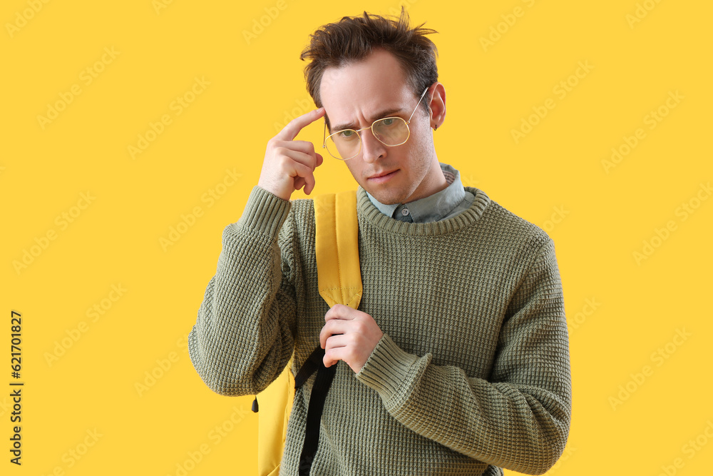 Thoughtful male student on yellow background