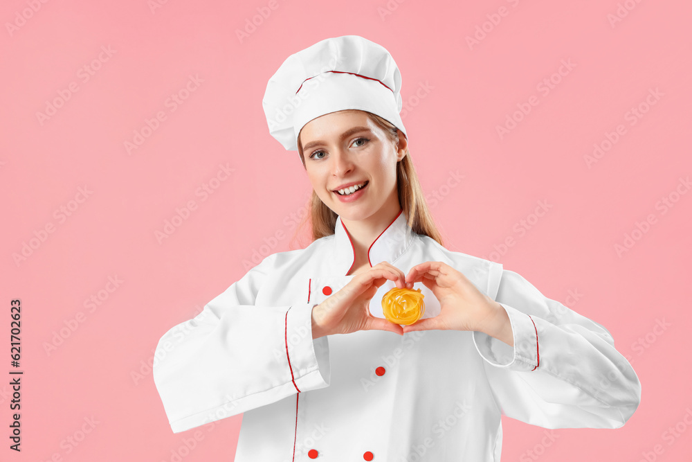 Female chef with raw pasta making heart on pink background