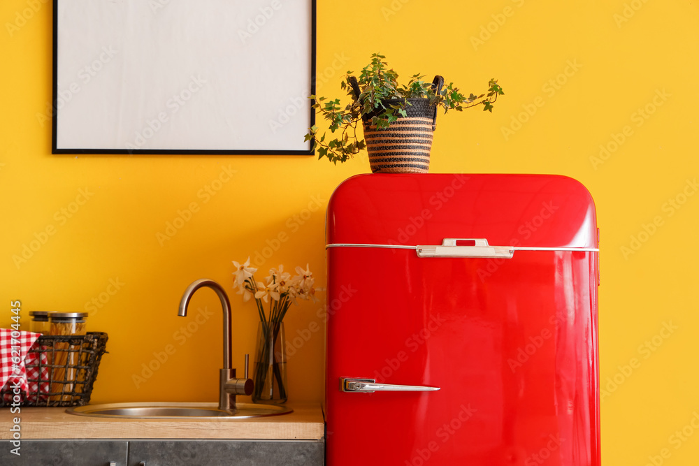 Interior of stylish kitchen with red fridge, blank picture and houseplant