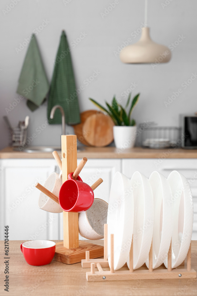 Holders with cups and plates on table in light kitchen, closeup