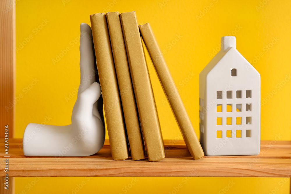 Stylish bookend and candle holder on shelf near yellow wall