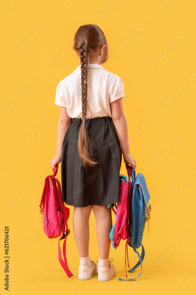 Little schoolgirl with backpacks on yellow background, back view