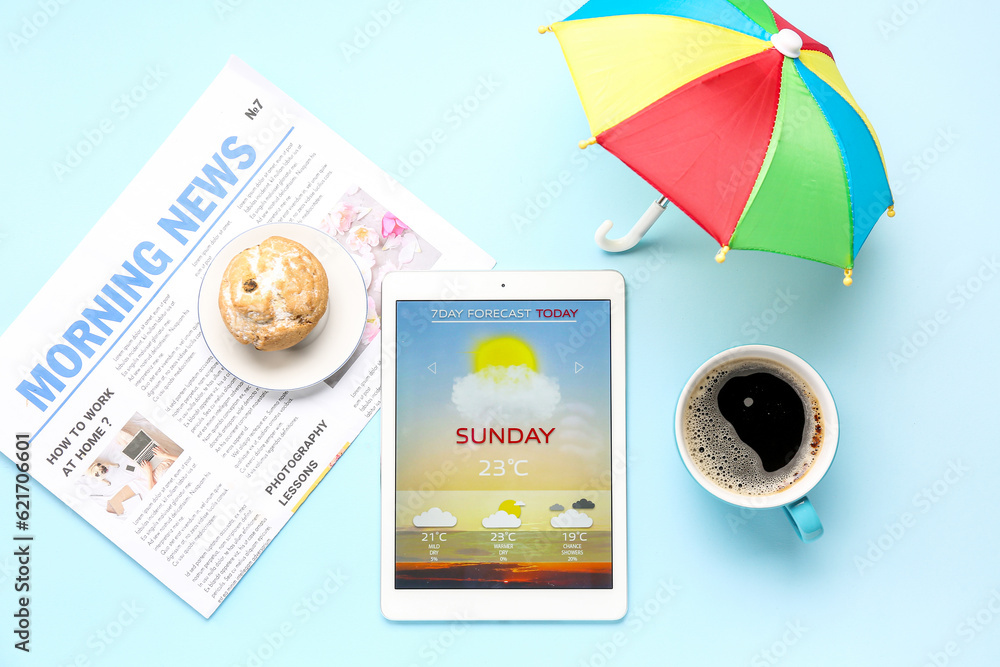 Tablet computer with weather forecast, muffin, coffee cup, newspaper and umbrella on blue background