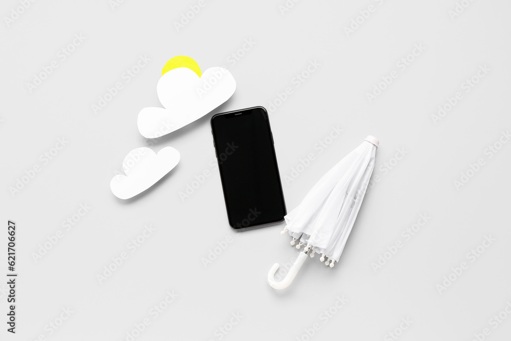 Mobile phone with umbrella and paper clouds on light background. Weather forecast concept