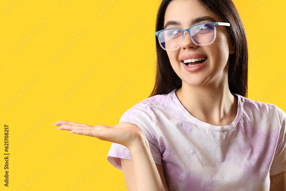 Pretty young woman wearing glasses and showing something on yellow background