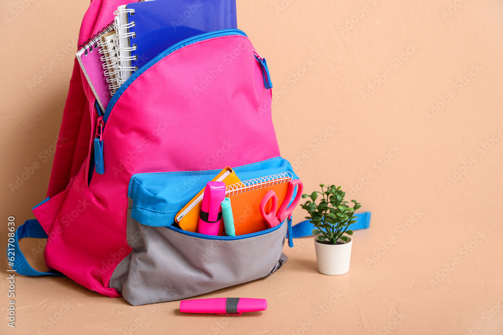 Color school backpack with notebooks, houseplant and markers on table near beige wall