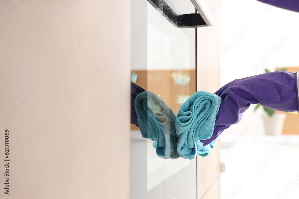 Woman cleaning electric oven with sponge in kitchen, closeup