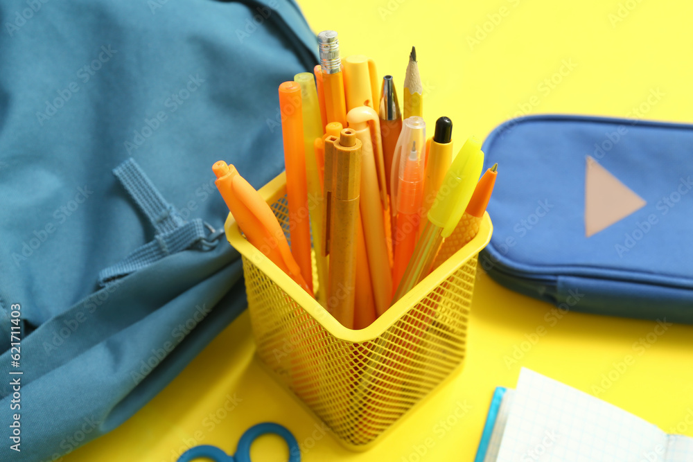 Cup with stationery and school backpack on yellow background, closeup