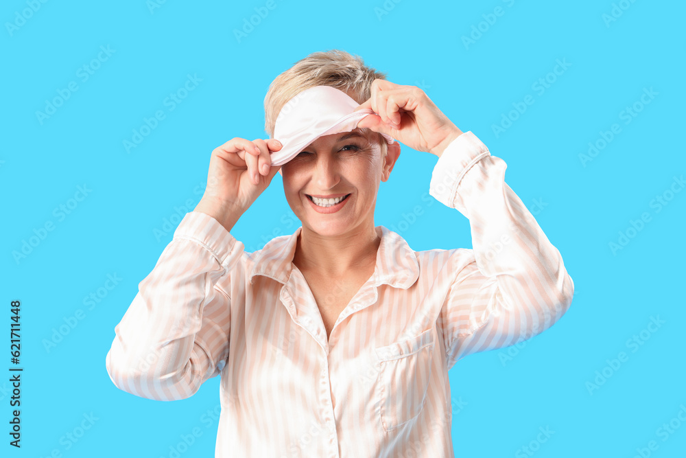 Mature woman in pajamas with sleeping mask on blue background