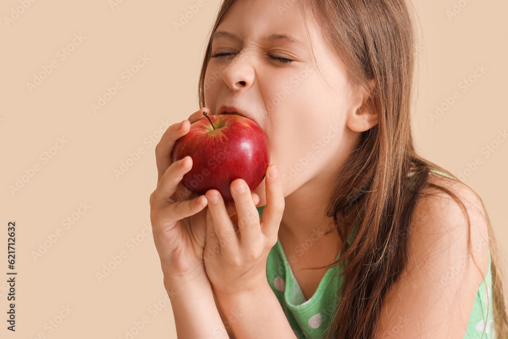 Little girl eating apple on beige background, closeup