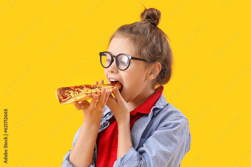 Little girl eating tasty pizza on yellow background