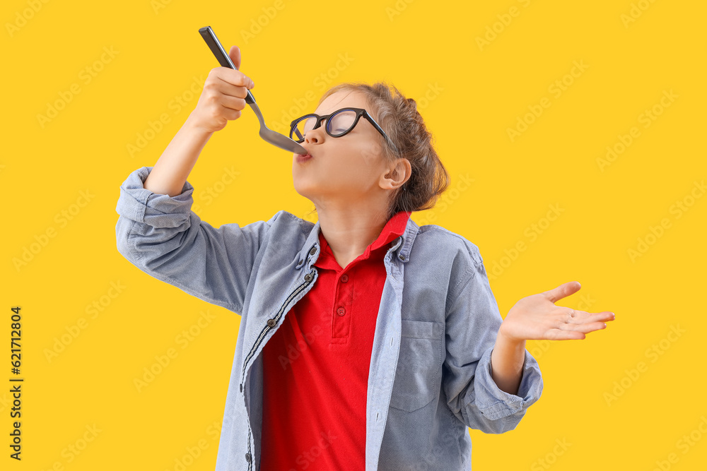 Little girl with spoon on yellow background