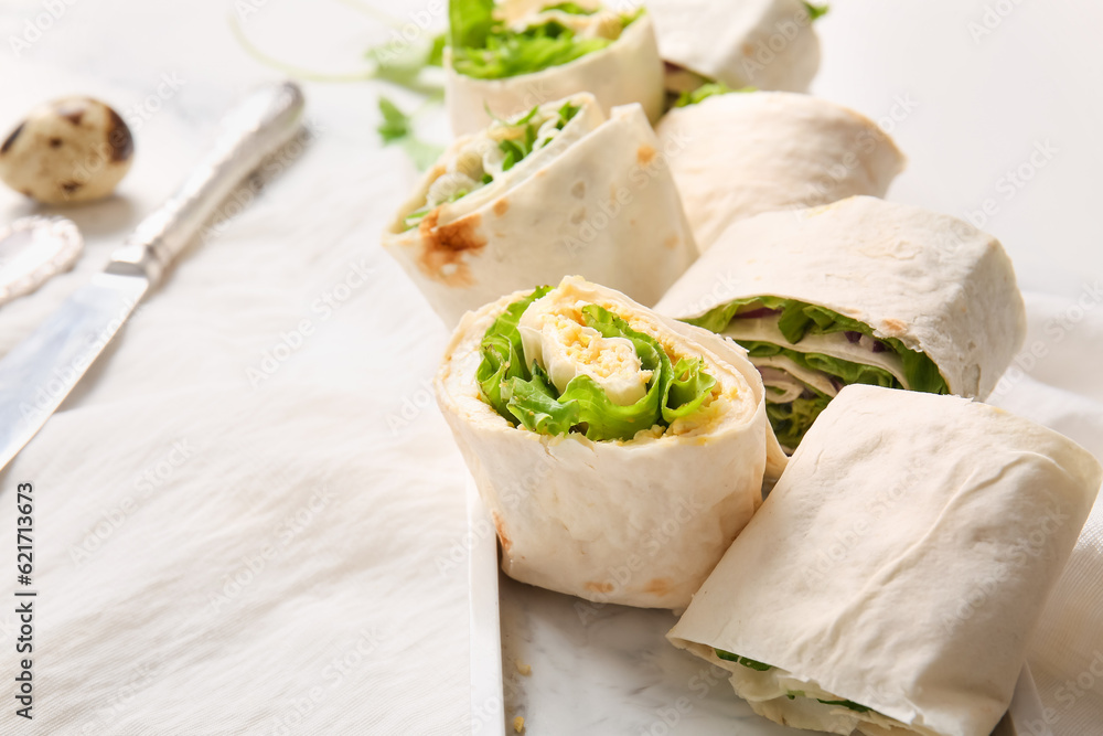 Plate of tasty lavash rolls with egg, onion and greens on white marble background