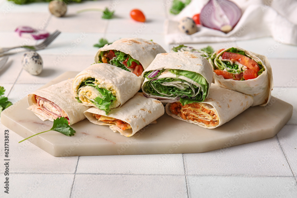 Board of tasty lavash rolls with vegetables on white tile background