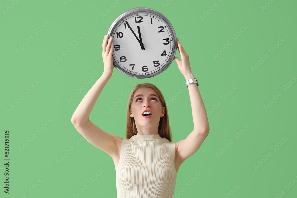 Stressed young woman with clock on green background. Deadline concept