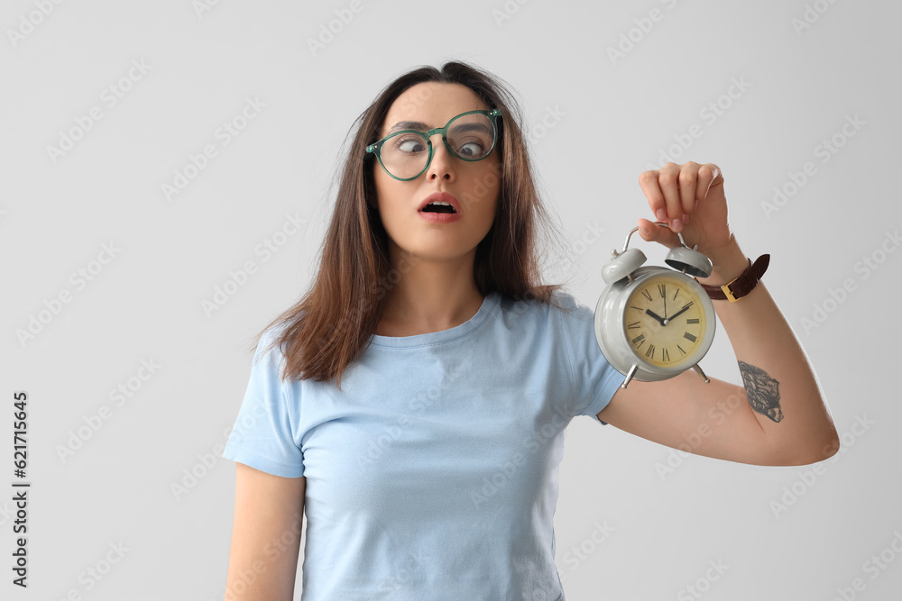 Stressed young woman with alarm clock on light background. Deadline concept